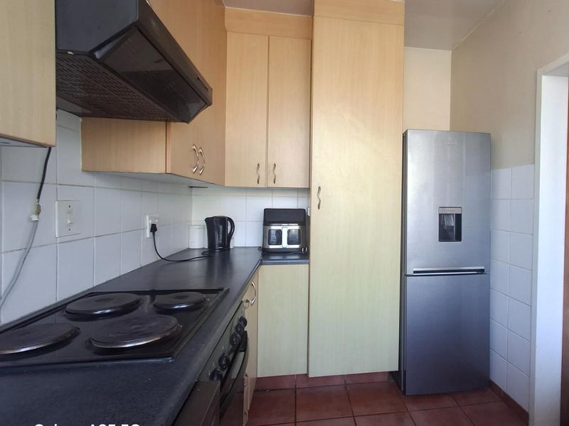 A functional kitchen featuring light wood cabinetry, a dark countertop, electric hob with extractor fan, and tiled flooring.