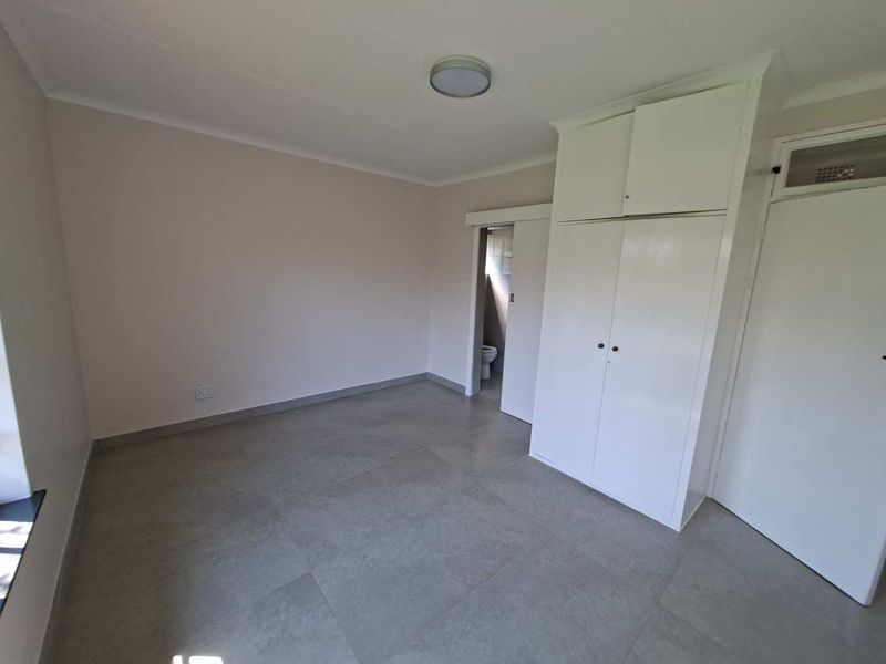 A clean, empty bedroom featuring neutral tiled flooring, built-in cupboards, and a sliding door leading to an en-suite bathroom.