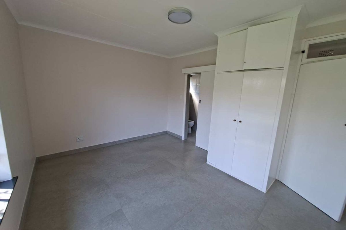 A clean, empty bedroom featuring neutral tiled flooring, built-in cupboards, and a sliding door leading to an en-suite bathroom.
