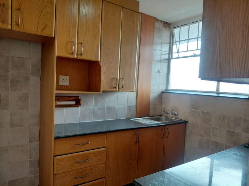 A dated kitchen featuring wooden cabinetry, laminate countertops, and a tiled backsplash, requiring cosmetic updates to modernize the space.