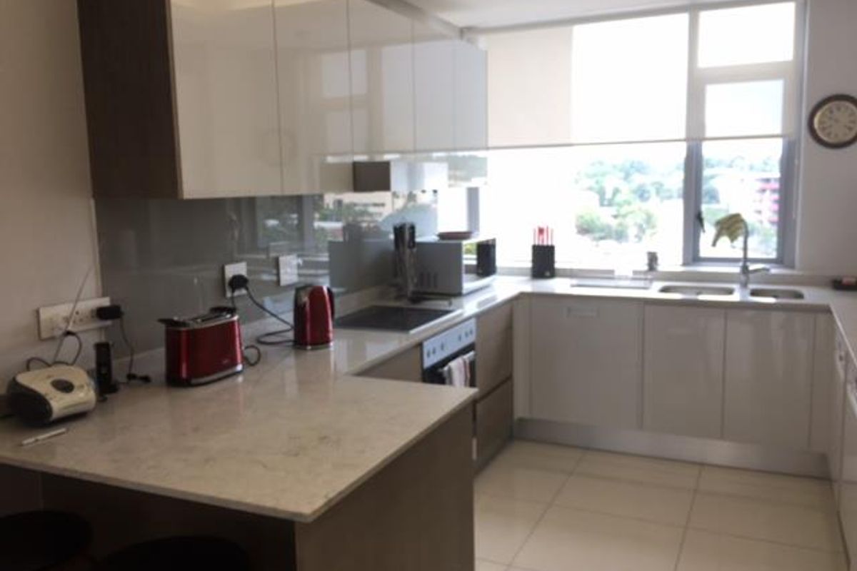Modern kitchen featuring high-gloss cabinetry, stone countertops, integrated appliances, and large windows providing ample natural light and an urban view.