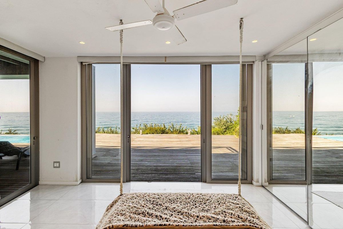 Bright living area featuring large sliding glass doors that open onto a wooden deck with panoramic ocean views.