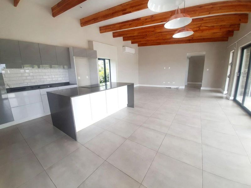 Spacious open-plan living and kitchen area featuring modern cabinetry, a central island, exposed timber beams, and large sliding doors leading to the exterior.