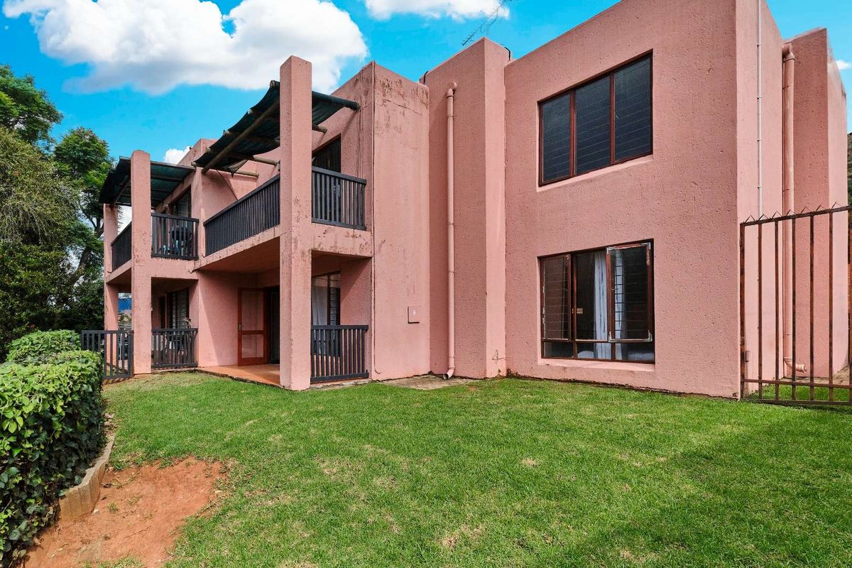 Rear view of a two-story townhouse featuring a private garden, covered balconies, and textured pink exterior walls.