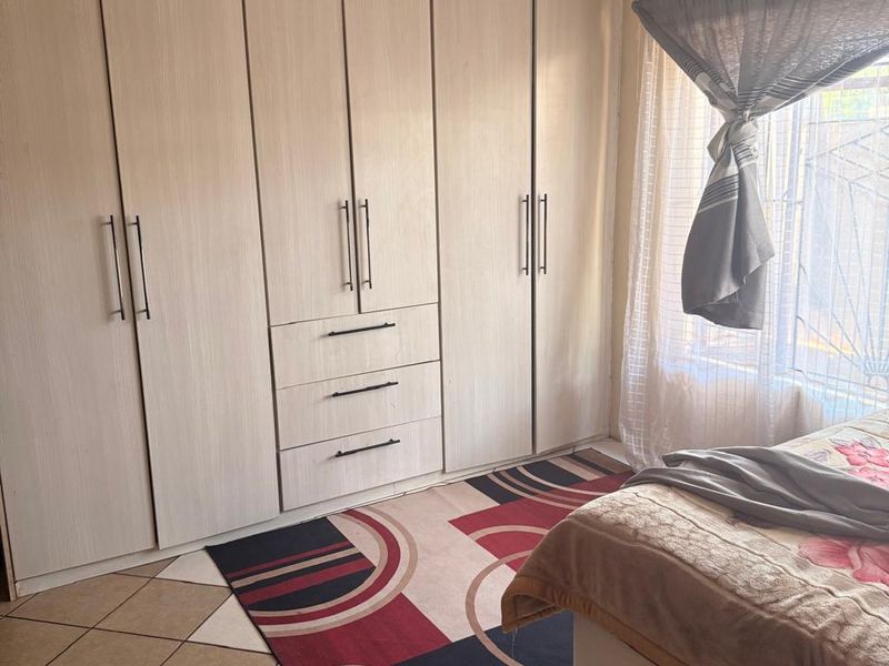 A bedroom featuring light-toned built-in cupboards with integrated drawers and tiled flooring, complemented by natural light from the window.