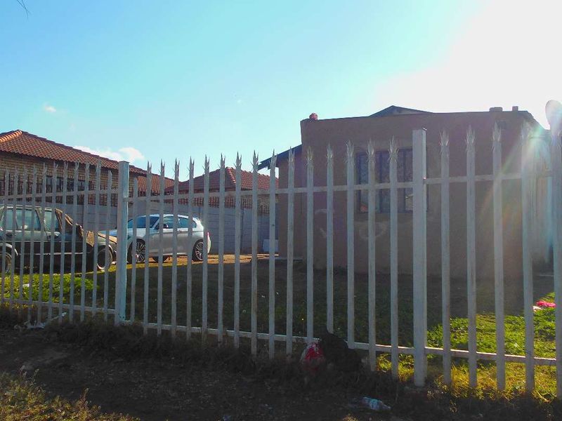 Front view of a residential property featuring a metal security fence and tiled roof, showing signs of wear and exterior maintenance needs.