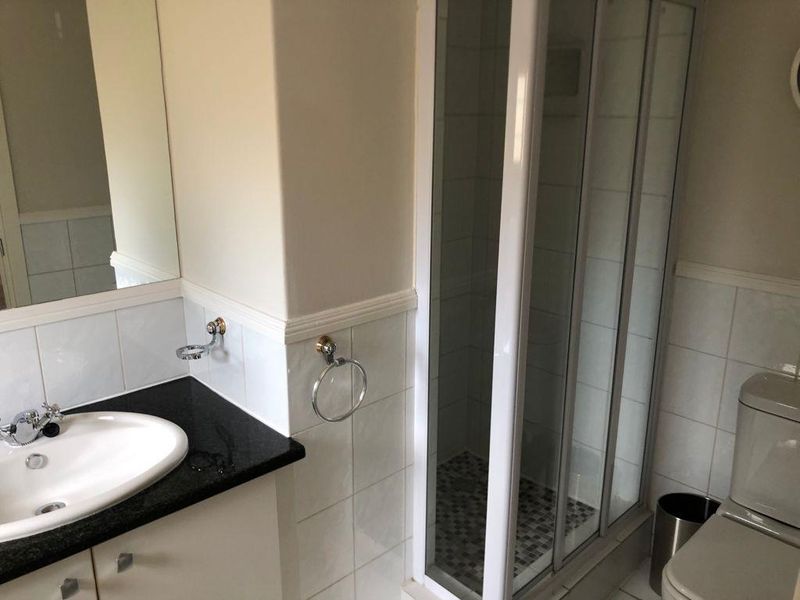 A functional bathroom featuring a shower enclosure, vanity basin with granite countertop, and a toilet, finished with tiled splashbacks.