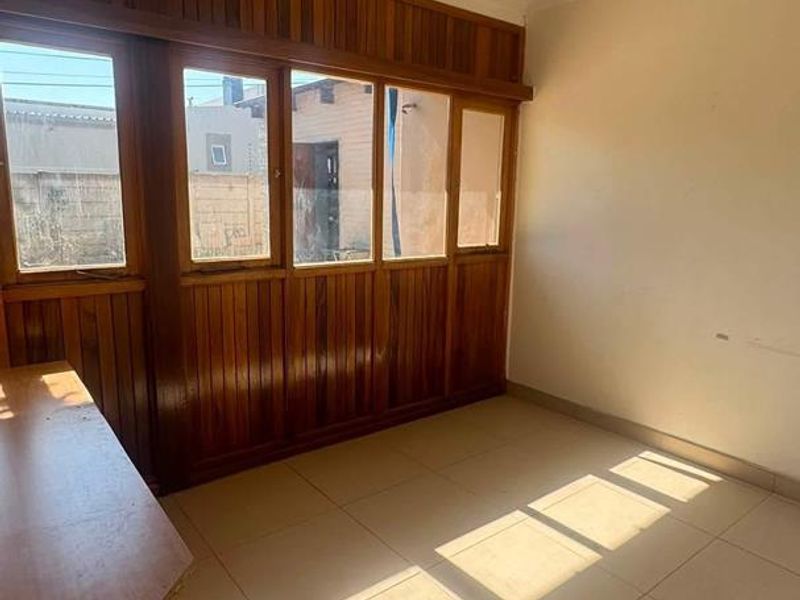An empty living area featuring tiled flooring, a ceiling fan, and extensive timber wall paneling under the windows.