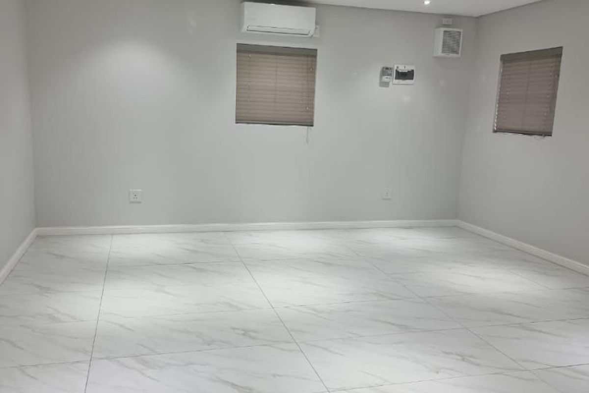 A bright, open-plan retail space featuring modern marble-look floor tiles, recessed downlighting, and a wall-mounted air conditioning unit.