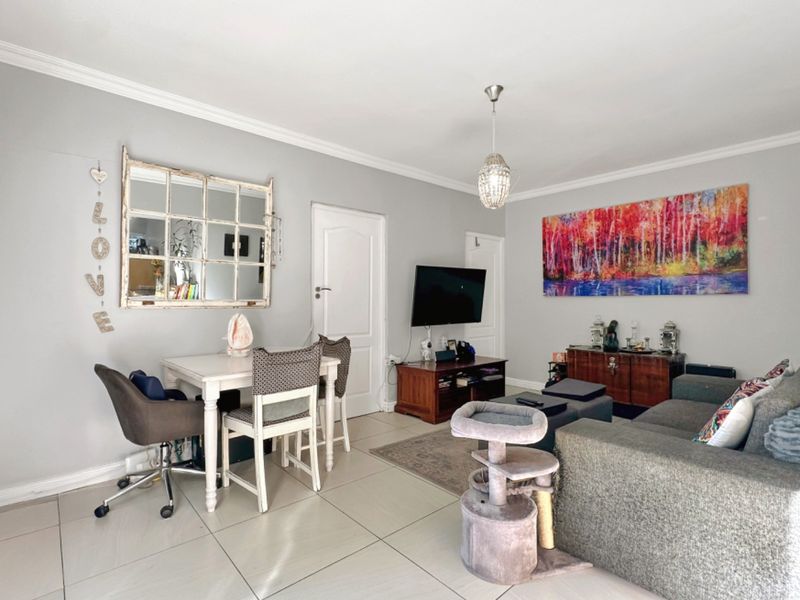 A well-maintained living room featuring neutral tiled flooring, cove cornicing, and a central pendant light fixture, providing a bright and functional living space.