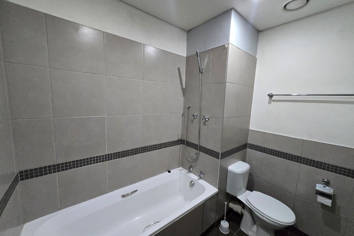 A clean, functional bathroom featuring a built-in bathtub with a handheld shower attachment, a standard toilet, and neutral wall and floor tiling.