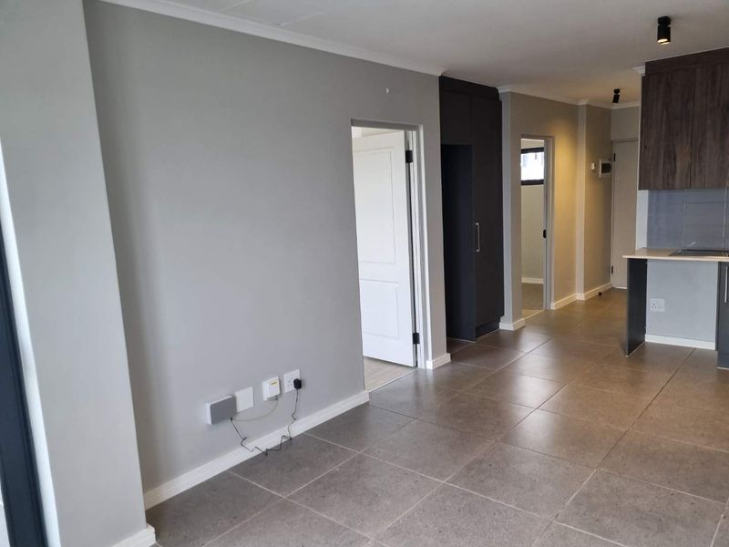 An open-plan living and kitchen area featuring modern grey tiled flooring, neutral wall tones, and contemporary built-in cabinetry.