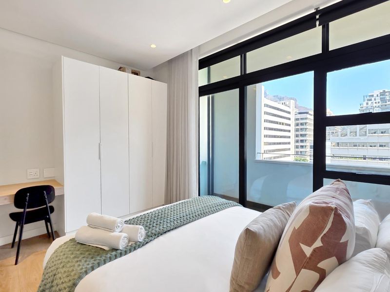 Modern bedroom featuring a built-in wardrobe, integrated desk, and large sliding glass doors that provide ample natural light and access to a balcony.