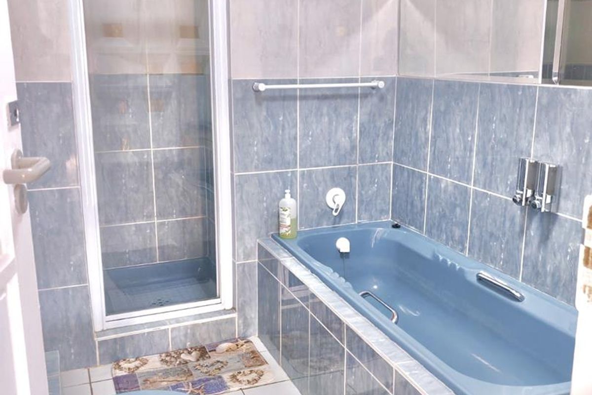 A functional bathroom featuring a built-in blue bathtub, a separate shower enclosure, and full-height wall tiling.
