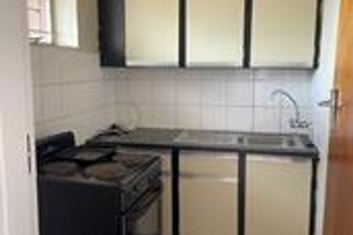 A compact kitchen featuring built-in cabinetry, a tiled backsplash, a stainless steel sink, and tiled flooring.