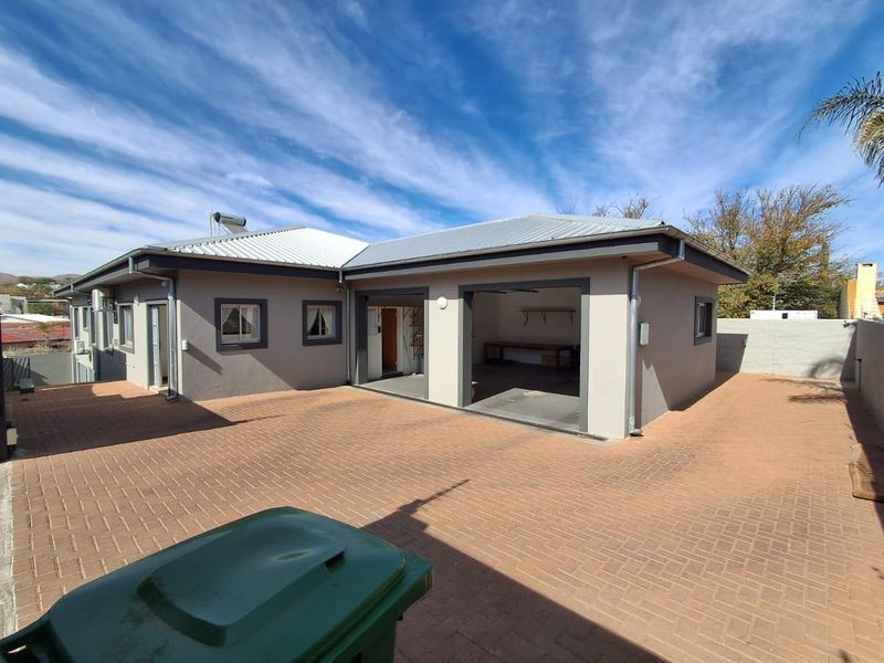 Rear view of the property featuring a paved courtyard, a double garage, and a solar water heating system on the metal roof.