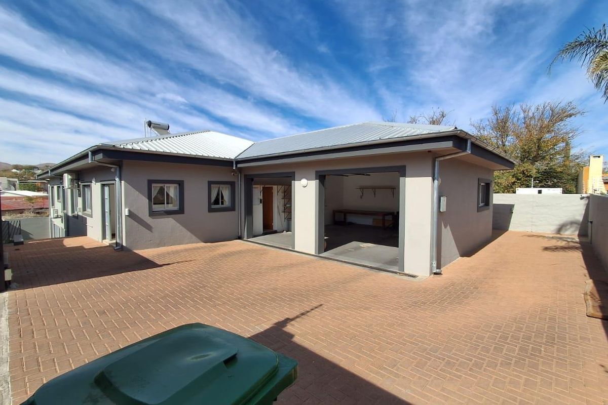 Rear view of the property featuring a paved courtyard, a double garage, and a solar water heating system on the metal roof.