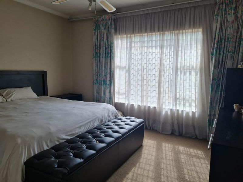 A standard bedroom featuring carpeted flooring and a ceiling fan, with large windows allowing for natural light.