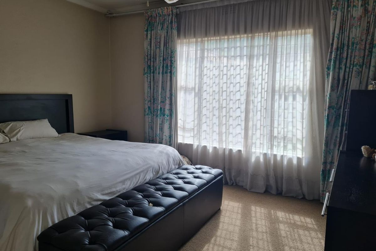 A standard bedroom featuring carpeted flooring and a ceiling fan, with large windows allowing for natural light.
