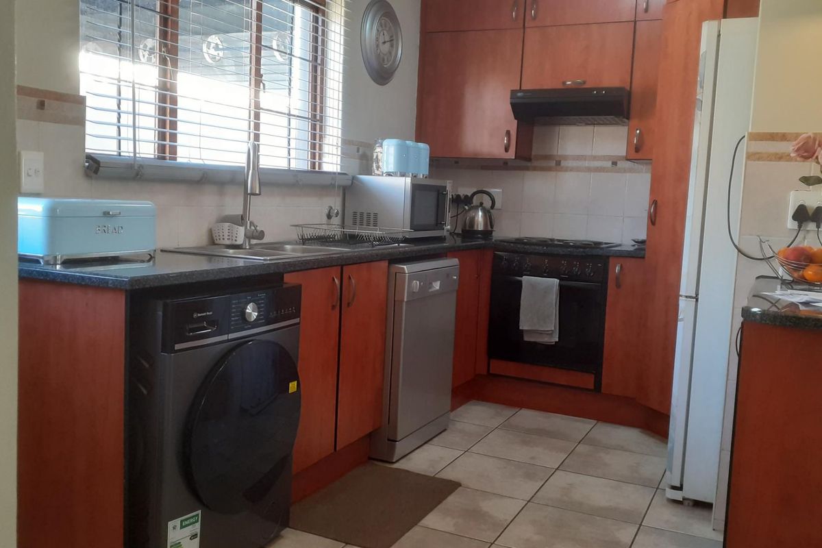 Functional kitchen featuring wood-finish cabinetry, dark laminate countertops, tiled backsplash, and integrated cooking appliances with tiled flooring.