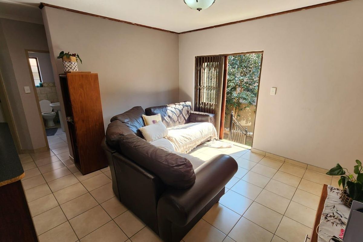 A living room featuring tiled flooring and a sliding glass door with a security gate, providing direct access to the exterior.