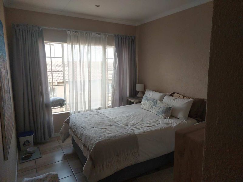 A functional bedroom featuring tiled flooring, neutral wall finishes, and a large window that provides natural light.