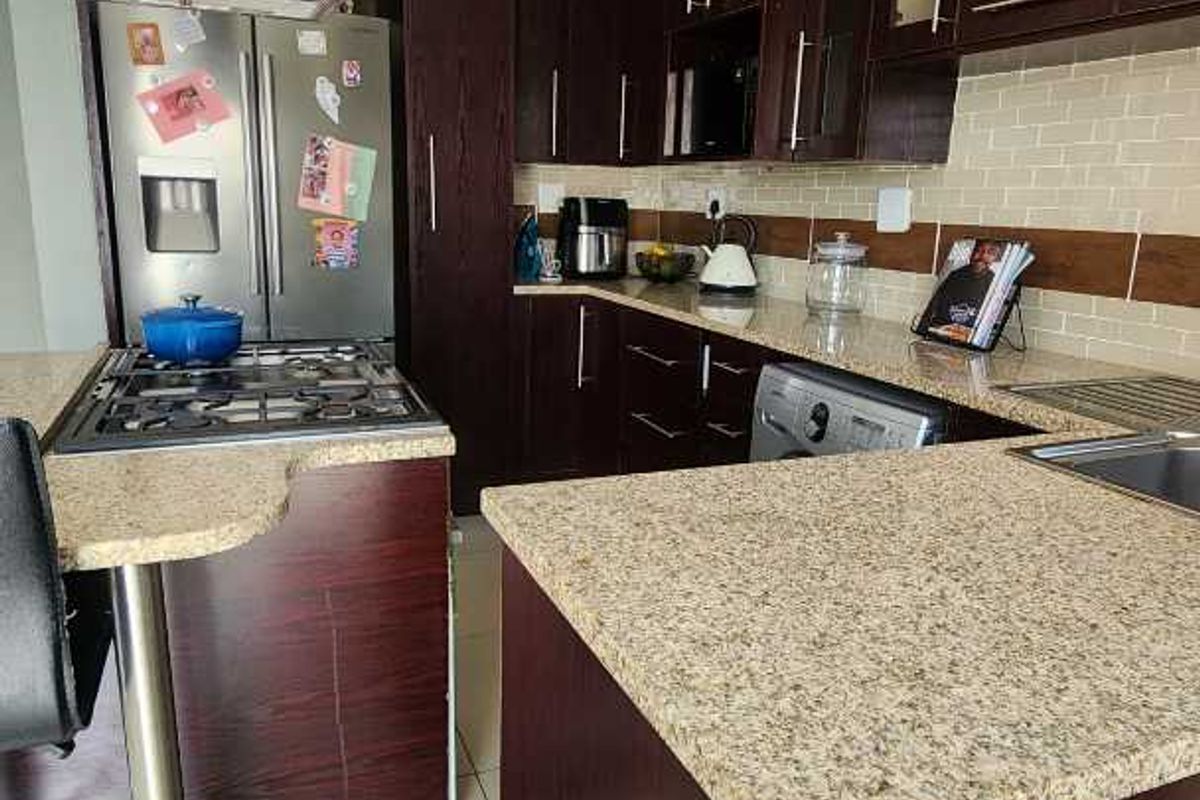 A functional kitchen featuring dark wood cabinetry, granite countertops, a gas hob with stainless steel extractor fan, and tiled flooring.