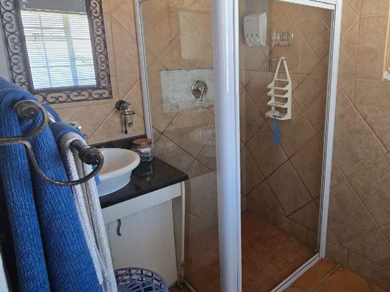 A compact bathroom featuring a shower enclosure, vanity basin, tiled finishes, and rustic exposed timber ceiling beams.