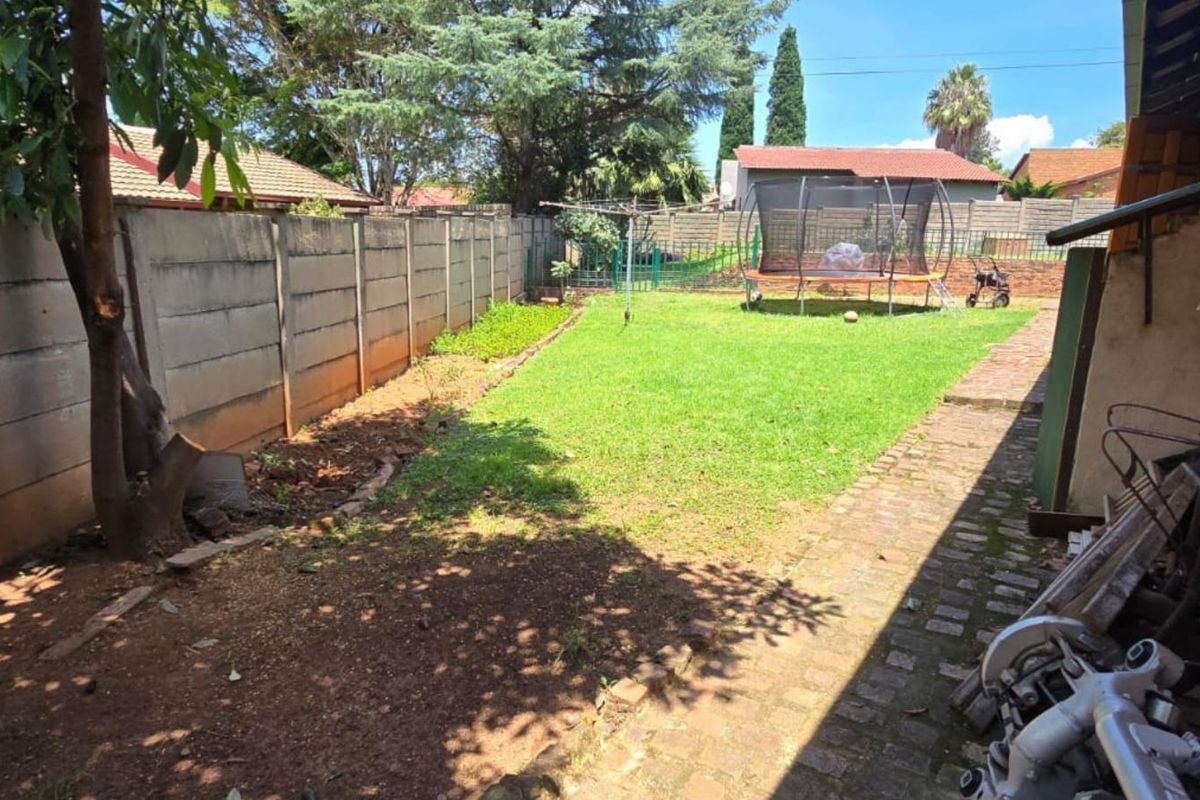 A rear garden area featuring a lawn, brick paved walkway, and precast concrete boundary walling.