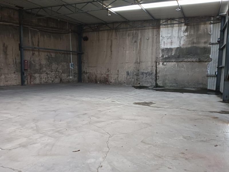 Spacious industrial warehouse unit featuring high ceilings, exposed steel structural beams, concrete flooring, and natural light from overhead skylights.