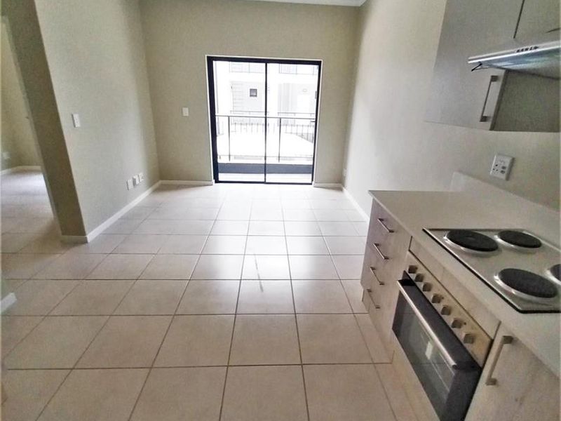 An open-plan kitchen and living area featuring tiled floors, built-in cabinetry with integrated appliances, and a sliding door leading to a balcony.