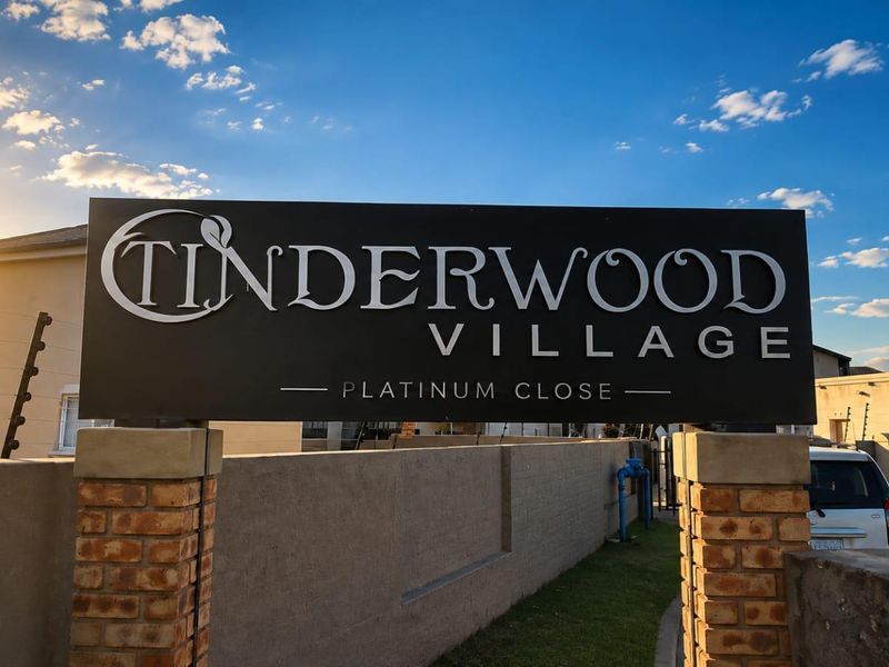 Entrance signage for Tinderwood Village, featuring brick pillars and perimeter walling with integrated electric security fencing.