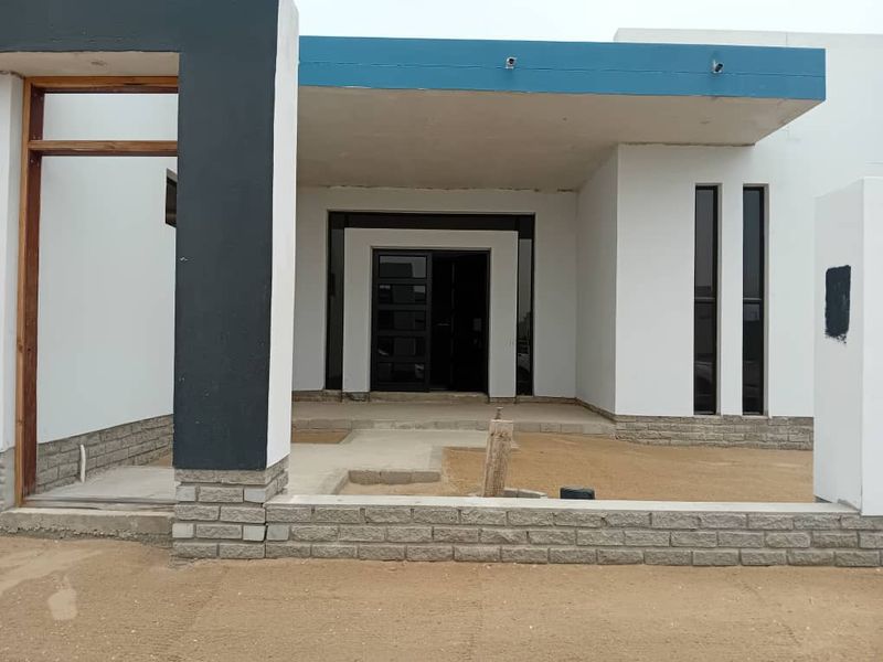 Modern front facade featuring stone cladding and a covered entrance, currently undergoing final exterior finishing and landscaping.