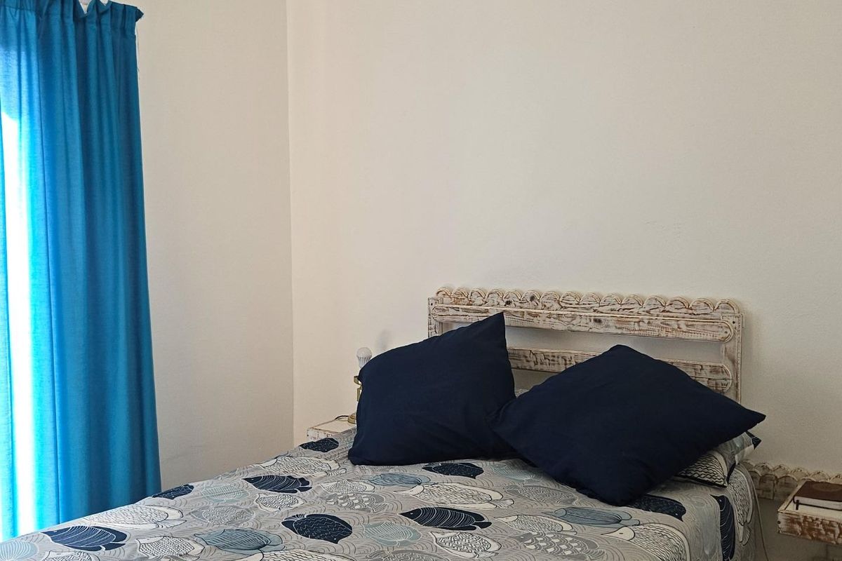 A bedroom featuring neutral walls and a window with blue curtains.