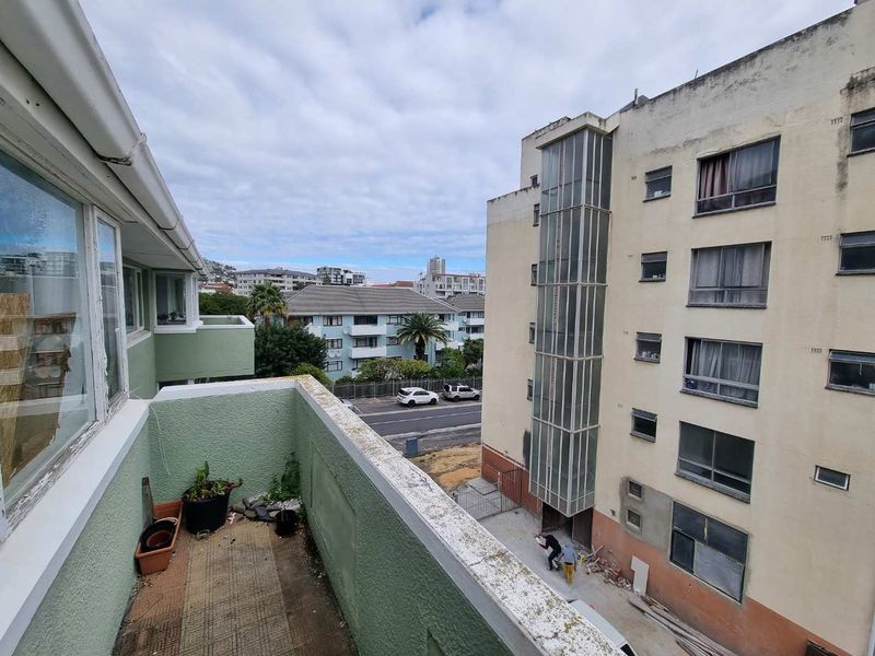 A balcony overlooking the surrounding apartment complex and street, featuring tiled flooring and painted masonry walls in need of maintenance.