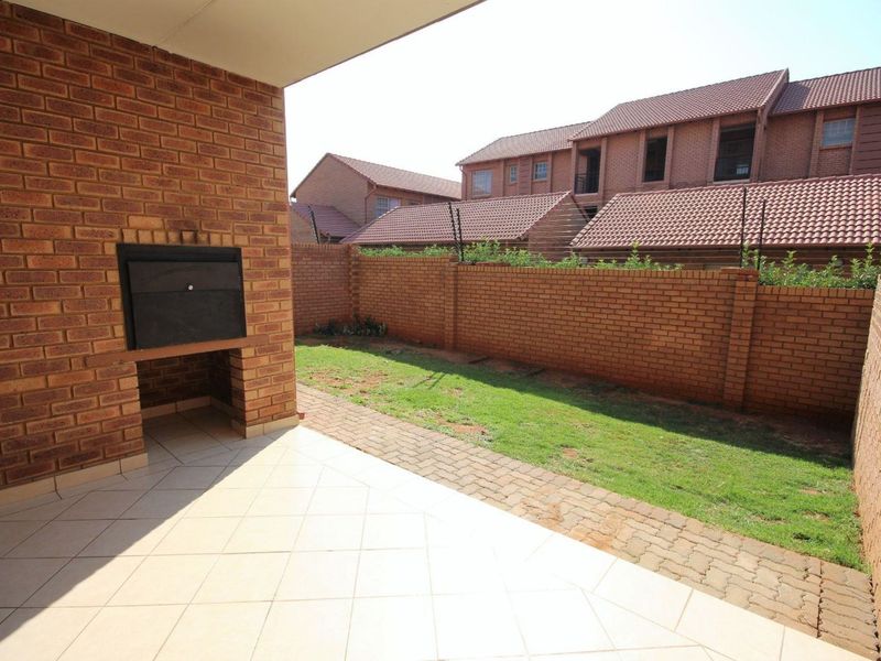 A covered patio area featuring a built-in braai, tiled flooring, and direct access to a private, enclosed garden space with brick boundary walls.