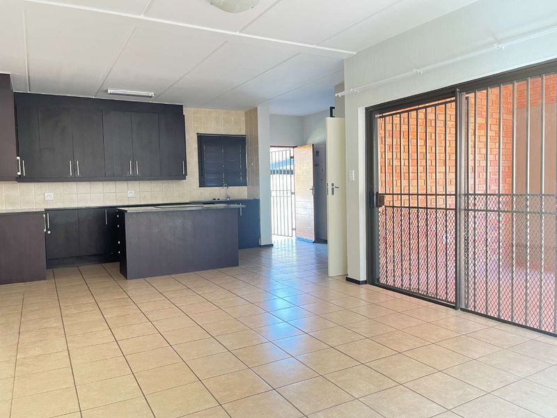 Open-plan living area featuring a kitchen with dark cabinetry, tiled flooring, and sliding doors leading to an outdoor space with security gates.