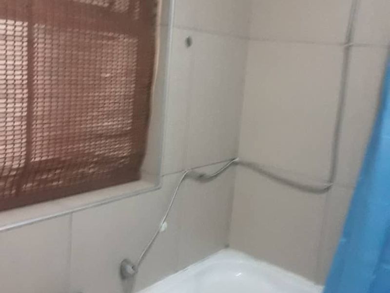 A bathroom featuring a bathtub with a shower attachment and tiled walls, currently showing signs of dated finishes and exposed plumbing.