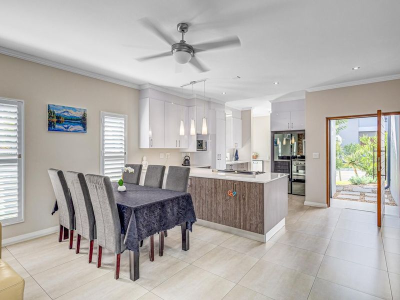 Modern open-plan kitchen and dining area featuring a central island, sleek cabinetry, tiled flooring, and direct access to the outdoor patio.