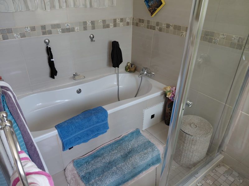 A functional bathroom featuring a built-in bathtub with a handheld shower attachment and a separate glass-enclosed shower area with neutral wall tiling.