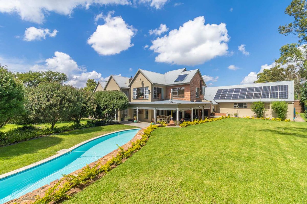 Spacious rear exterior view featuring a large landscaped garden, a long swimming pool, a covered patio area, and solar panels installed on the roof.