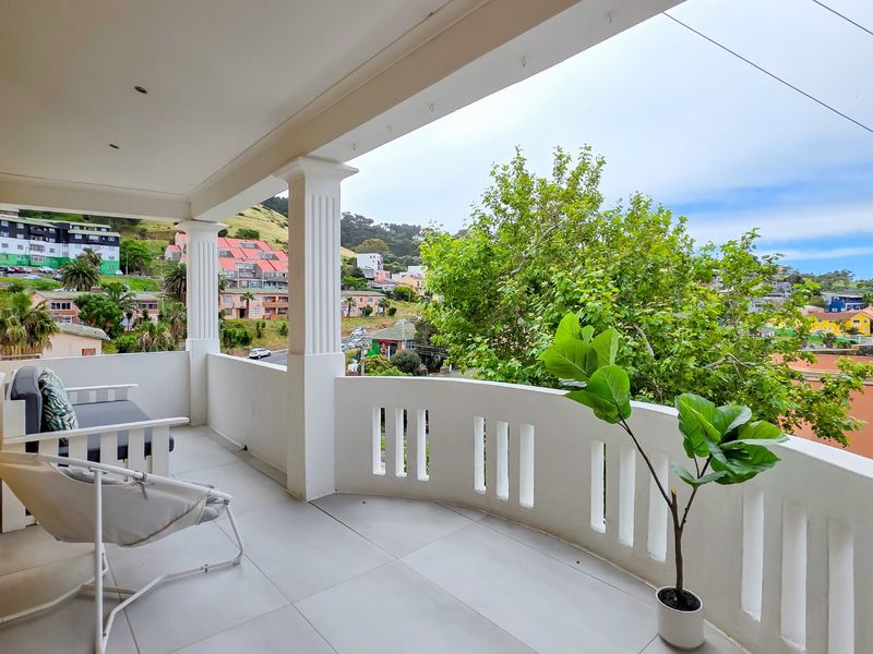 A spacious covered balcony featuring tiled flooring, decorative columns, and a solid balustrade, offering an elevated view of the surrounding neighborhood.
