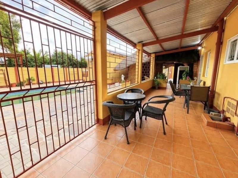 A covered outdoor patio area featuring tiled flooring, a corrugated metal roof, and a security gate overlooking the swimming pool.