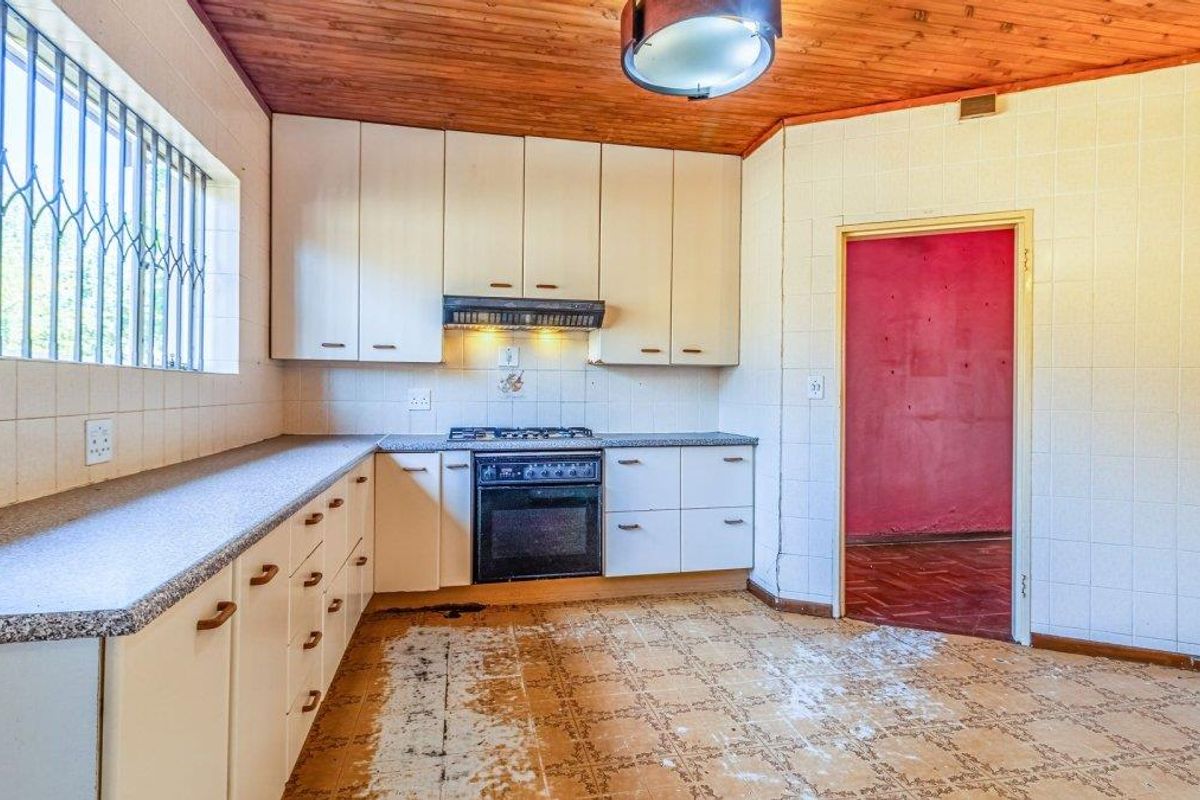 A dated kitchen featuring original cabinetry, a freestanding oven, and timber ceiling, requiring modernization to improve functionality and aesthetic appeal.