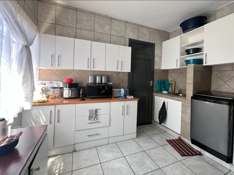 A functional kitchen featuring white cabinetry, laminate countertops, tiled backsplash, and tiled flooring, providing a practical workspace with integrated storage solutions.