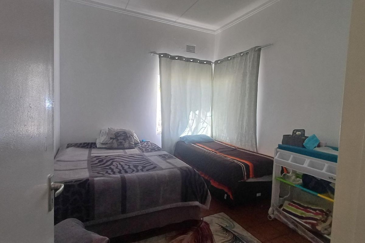 A bedroom featuring white walls, a corner window with curtains, and a ventilation grille.