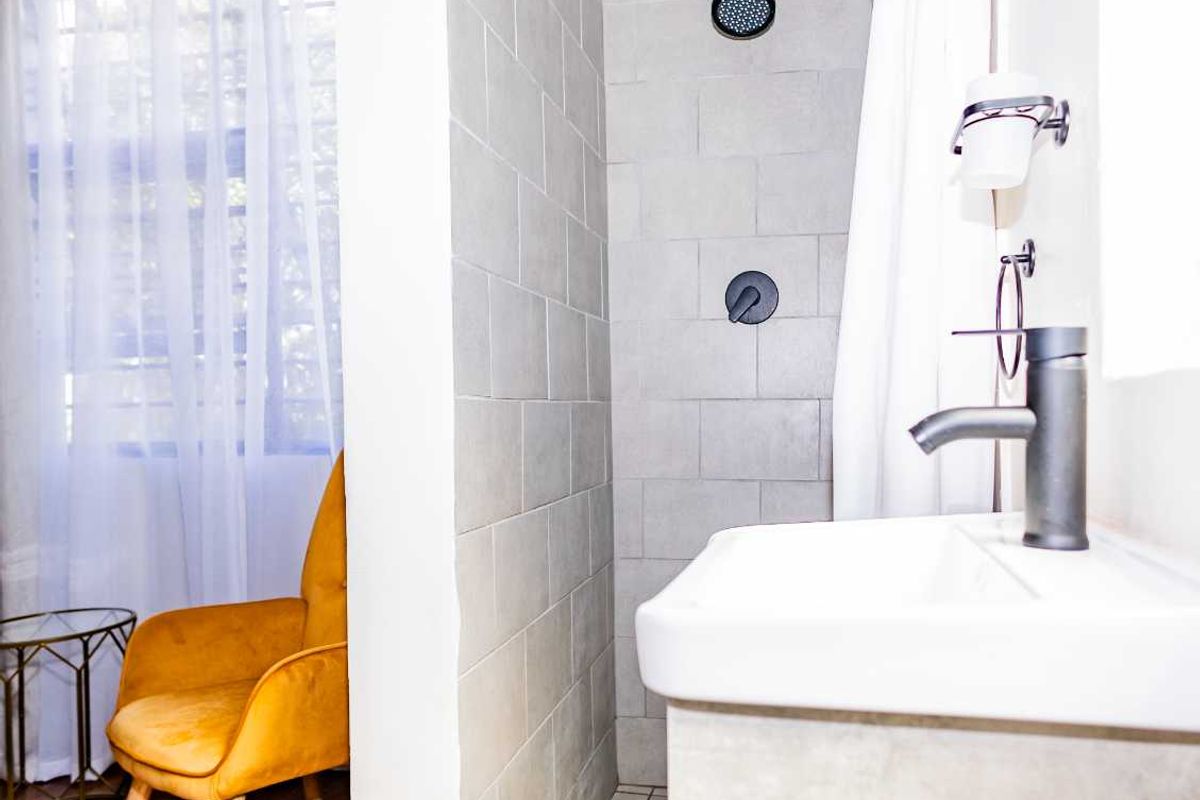 A modern bathroom featuring a walk-in shower with grey wall tiles, a contemporary vanity with a basin, and dark matte fixtures.