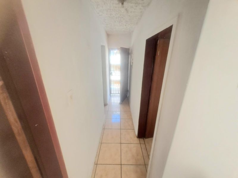 A narrow residential hallway featuring tiled flooring and textured ceiling, providing access to multiple rooms within the apartment.