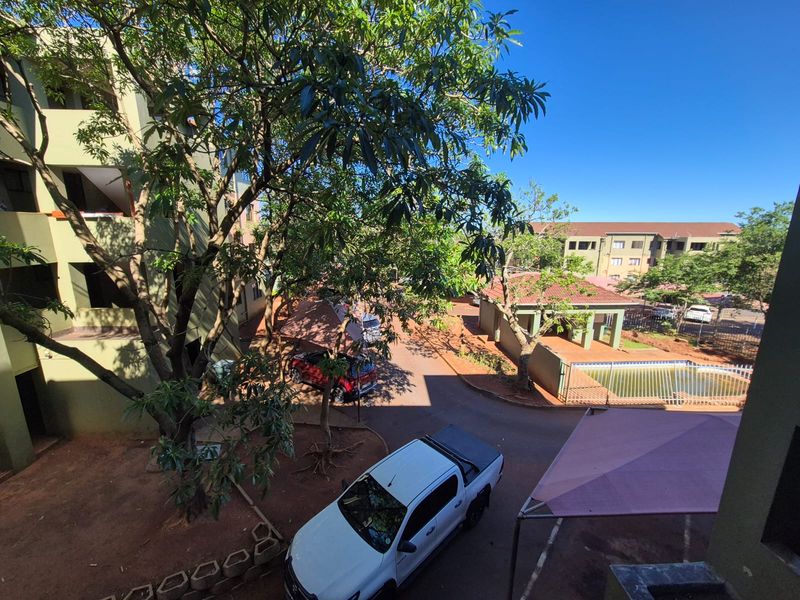 An elevated view of the apartment complex grounds, featuring a swimming pool, paved driveway, and mature trees within the residential estate.