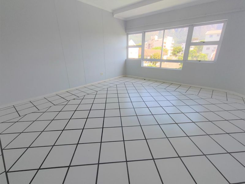 A bright, empty living area featuring large windows and distinctive diamond-patterned floor tiles, offering a blank canvas for interior design.